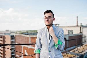 Dreamer stylish macho man in gray suit and glasses posed on the roof. photo