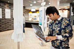 Young male indian freelancer sitting open laptop computer in fast food cafe, handsome asian man reading text message during work on net-book in comfortable coffee shop. photo