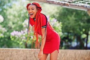 Cute and slim african american girl in red dress with dreadlocks in motion having fun on street. Stylish black model. photo
