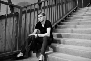 Young stylish macho boy in black jacket posed outdoor of street. Amazing model man at red stairs tonnel. photo