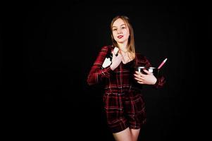 Young housewife in checkered dress with saucepan and kitchen spoon and bottle isolated on black background. photo