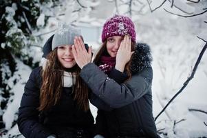 Two funny girls friends having fun at winter snowy day near snow covered trees. photo