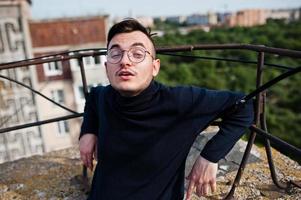 Dreamer stylish macho man in black golf and glasses posed on the roof. photo