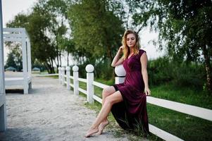 Blonde sensual woman in red marsala dress posing on beach of resort. photo