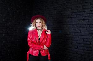 retrato de estudio de una chica rubia con sombrero rojo y chaqueta de cuero contra la pared de ladrillo. foto