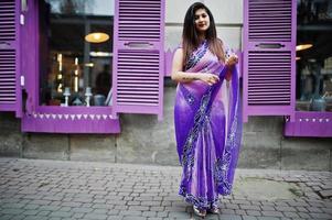 niña hindú india en el tradicional sari violeta posó en la calle contra ventanas moradas. foto