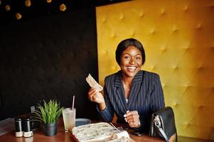 African american businesswoman eating cheese pizza in cafe. Black girl having rest. photo