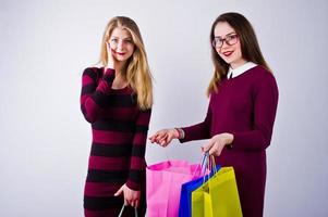 dos hermosas amigas con vestidos de cereza posando con bolsas de compras multicolores en el estudio. foto