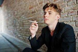 Young macho boy wear on blac stylish jacket smoking cigarette on streets. photo