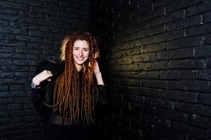 Studio shoot of girl in black with dreads and hat on brick background. photo