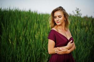 Blonde sensual woman in red marsala dress posing in the reeds. photo