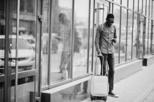 African american man in checkered shirt, with suitcase and backpack. Black man traveler against bus station.
