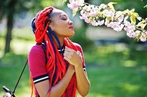 Linda y delgada chica afroamericana vestida de rojo con rastas posadas al aire libre en Spring Park. elegante modelo negro. foto