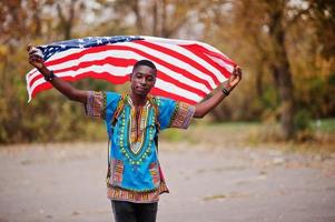 African man in africa traditional shirt on autumn park with USA flag. photo