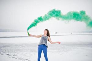 Young girl with green colored smoke bomb in hand in winter day. photo