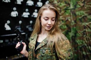 Military girl in camouflage uniform with gun at hand against army background on shooting range. photo