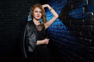 Curly hair girl at leather jacket on studio against black brick wall. photo