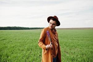 Stylish man in glasses, brown jacket and hat posed on green field. photo