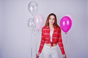 Young girl in red checked shirt and white pants with balloons against white background on studio. photo