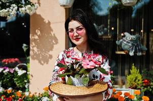 Summer portrait of brunette girl in pink glasses and hat against flowers shop. photo