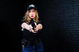 FBI female agent in cap and with gun at studio against dark brick wall. photo