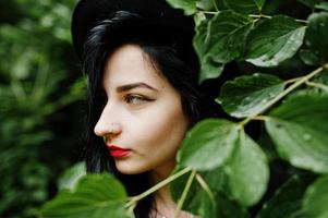 Close up portrait of sensual girl all in black, red lips and hat. Goth dramatic woman. photo