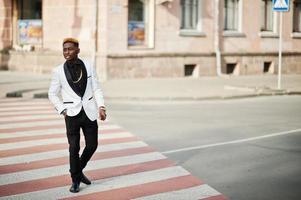 hombre afroamericano elegante y guapo con traje blanco caminando por el cruce de peatones. foto