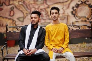 Two indian stylish mans friends in traditional clothes posed outdoor, sitting on bench. photo