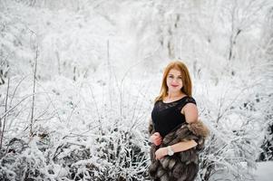 chica pelirroja con abrigo de piel caminando en el parque nevado de invierno. foto