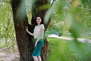 Brunette girl in green skirt and white blouse posed at park. photo