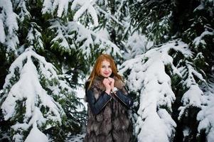 chica pelirroja con abrigo de piel caminando en el parque nevado de invierno. foto