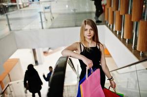 chica con bolsas de compras en el centro comercial en la escalera mecánica. foto