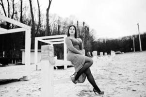 retrato de una chica morena vestida de gris sentada en una construcción de madera blanca. foto