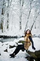 Elegance curly girl in fur coat at snowy forest park at winter. photo