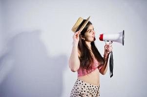 retrato de una hermosa joven en traje de baño y sombrero habla por megáfono en el estudio. foto