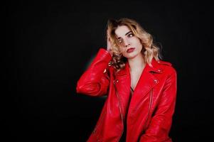 Studio portrait of blonde girl in red leather jacket against black background. photo