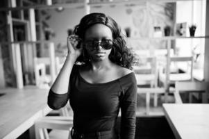 chica afroamericana con gafas de sol posadas en un café moderno. foto
