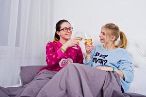 Two friends girls in pajamas having fun on bed at room. photo