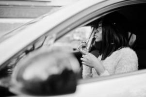 African american woman at violet dress and cap posed at yellow car and draws her lips. photo