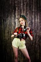 Young funny housewife in checkered shirt and yellow shorts pin up style with saucepan on wooden background. photo