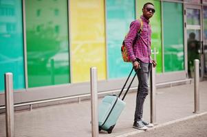 African american man in checkered shirt, sunglasses and jeans with suitcase. Black man traveler. photo