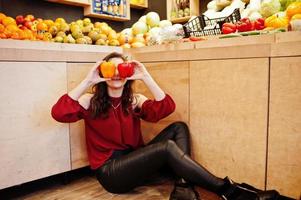 chica de rojo sosteniendo dos pimientos en la tienda de frutas. foto