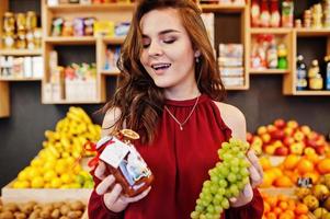 Girl in red holding grape jam in a jar on fruits store. photo
