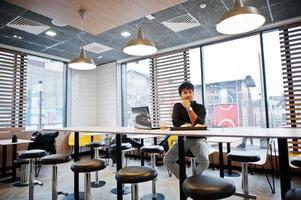 Stylish indian man sitting at fast food cafe against his laptop. photo