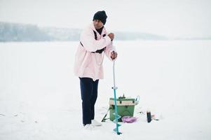 pescador afroamericano haciendo un agujero en el hielo congelado con un taladro. pesca de invierno. foto