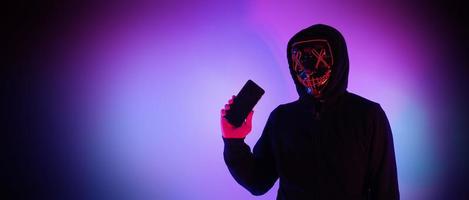 Anonymous hacker and face mask with smartphone in hand. photo