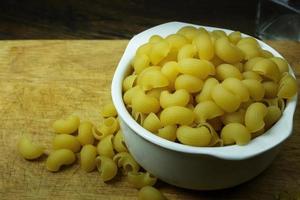 Macaroni raw in white bowl on wood table photo