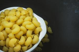Macaroni raw in white bowl on black plate. photo