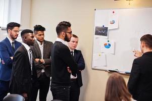 Multiracial business team addressing meeting around boardroom table and write plan on board. photo