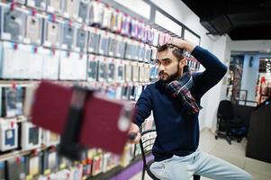 Indian man customer buyer at mobile phone store making selfie by smartphone on monopod stick. South asian peoples and technologies concept. Cellphone shop. photo